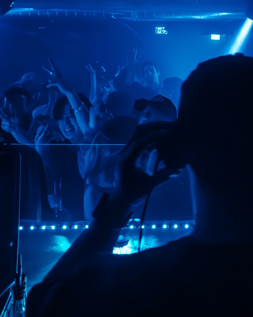 Crowd with hands up in deep blue light at De:code
